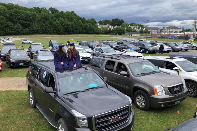 Two Essex graduates sit on their sunroof in a parking lot at graudation