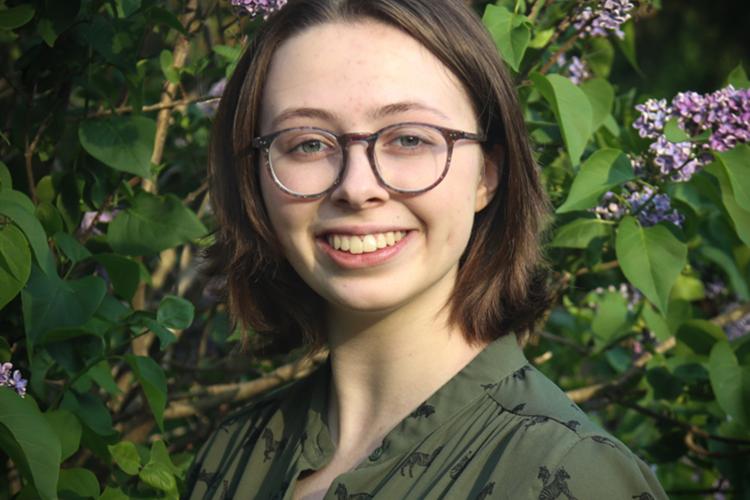 Abby smiling standing in front of a lilac tree.