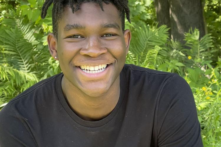 OJ Daring smiling sitting outside with green plants behind him