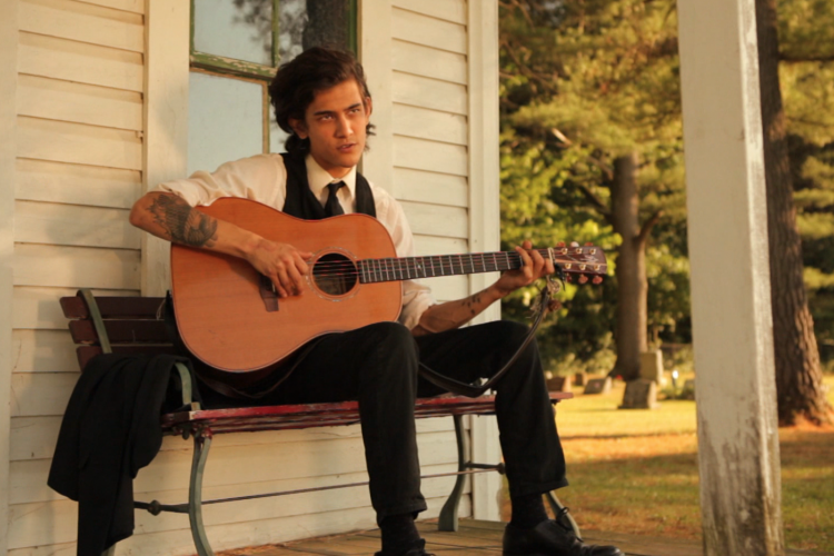 Still from Give Love To Get Love of a person playing guitar on a cottage porch