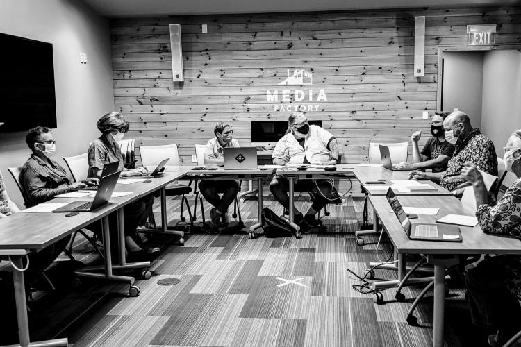 Board members sit around a table in the Media Factory at a monthly meeting.