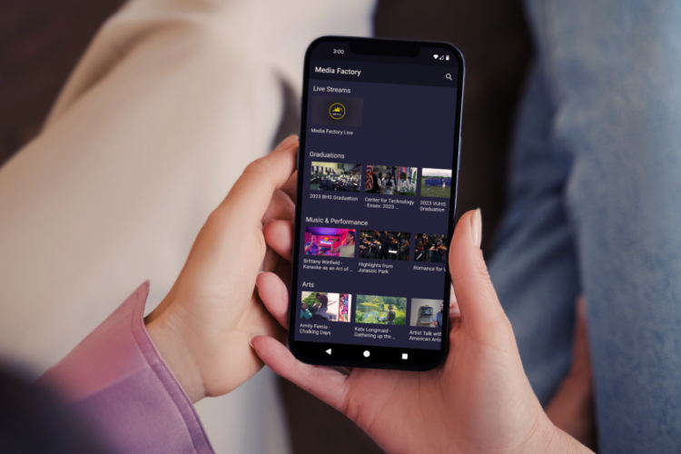 two hands holding a phone with the Media Factory channel visible.