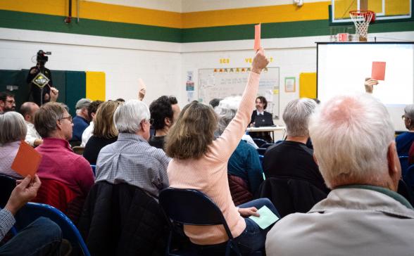People holding up red cards at a town meeting