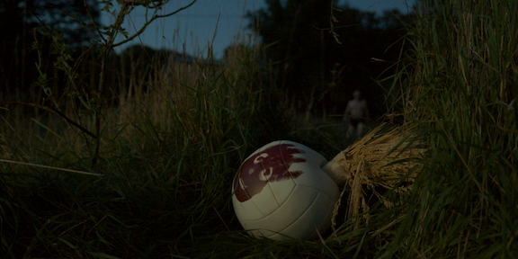 volleyball in foreground with man wearing raggedy shorts in far background