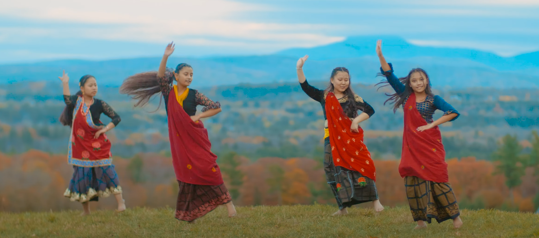 Still from Milan Magar's film of a performance of 4 girls dancing in red saris in a mountain setting