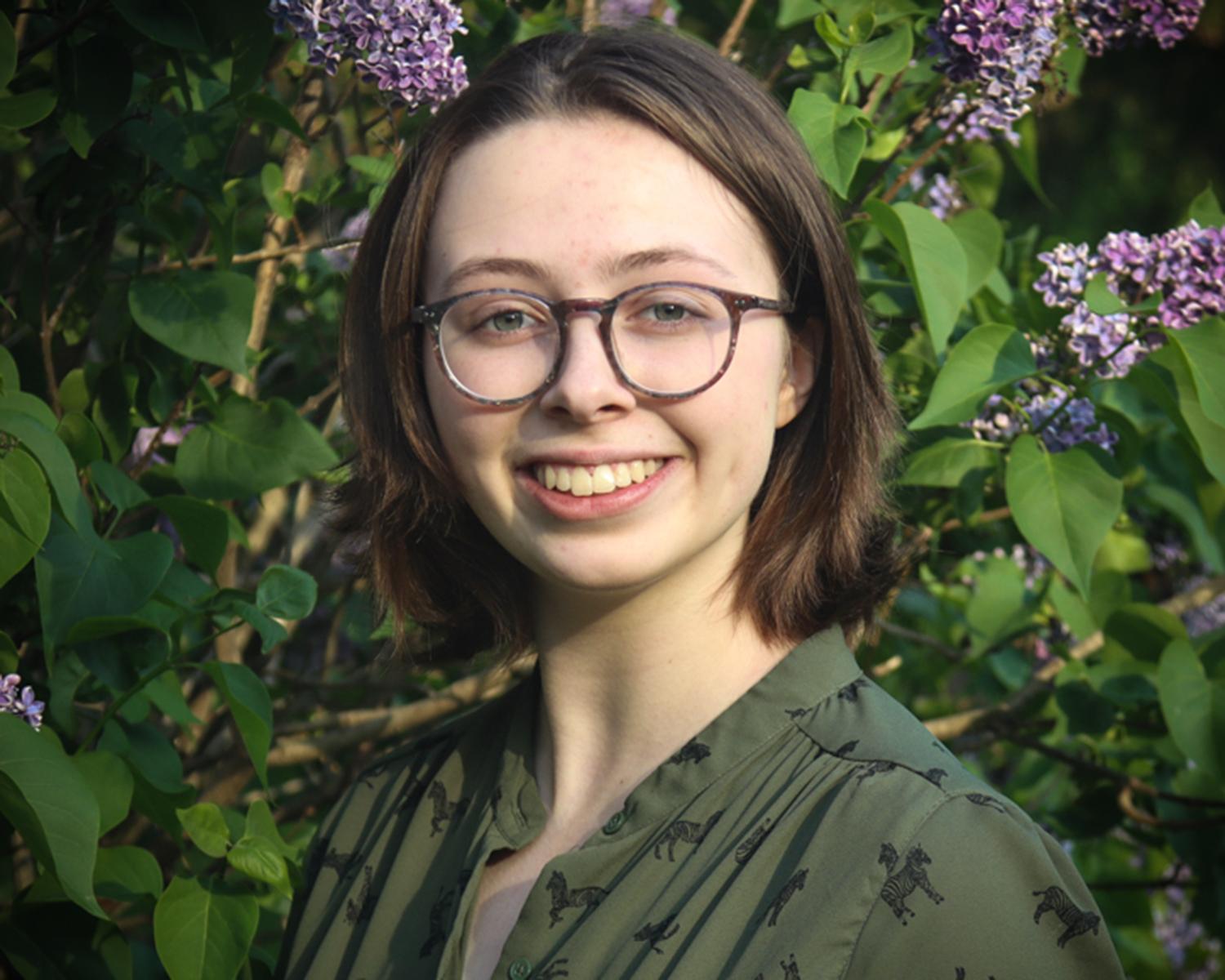 Abby smiling standing in front of a lilac tree.
