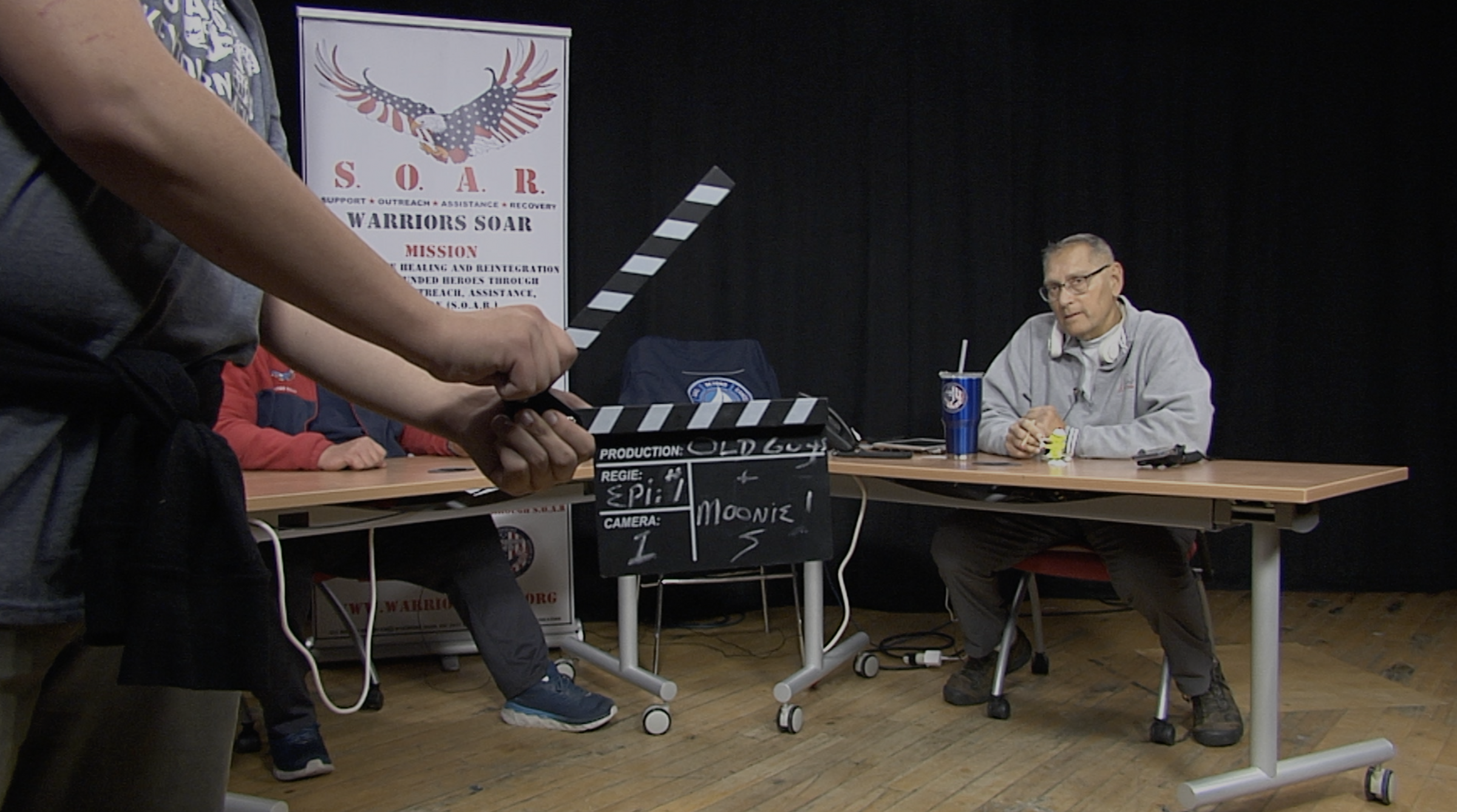 Steve Miliza ready to speak with hands holding clapboard in foreground.