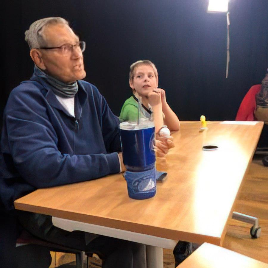 Steve sitting at a table with a child, talking.