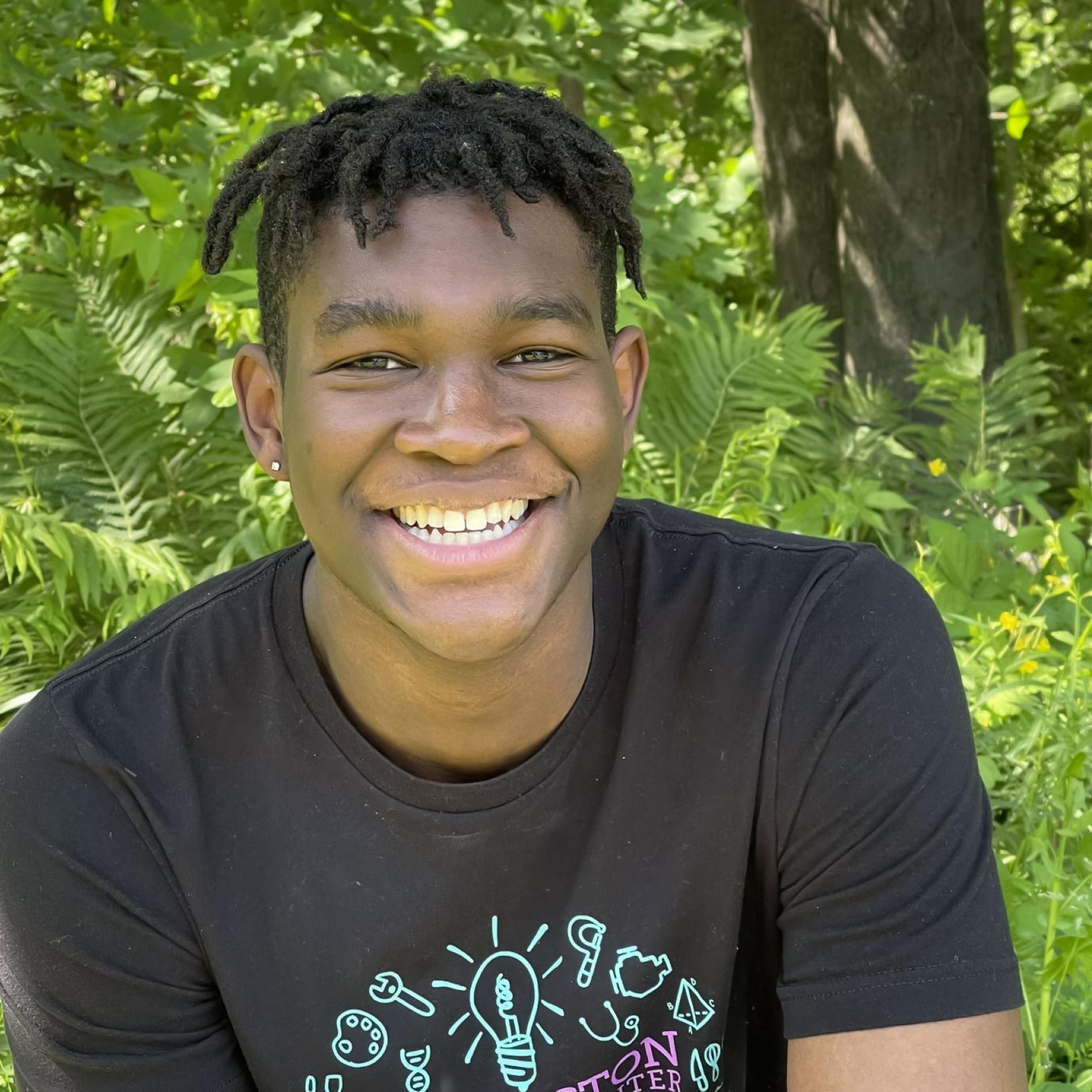 OJ Daring smiling sitting outside with green plants behind him