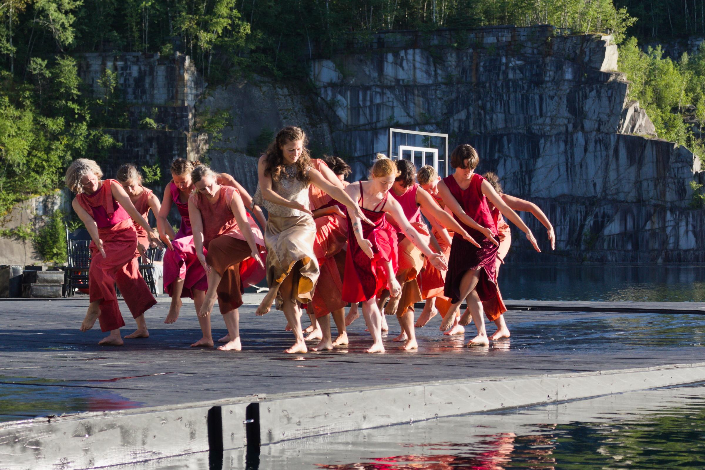 A group of dancers wearing red move together on a dock floating in a deep quarry