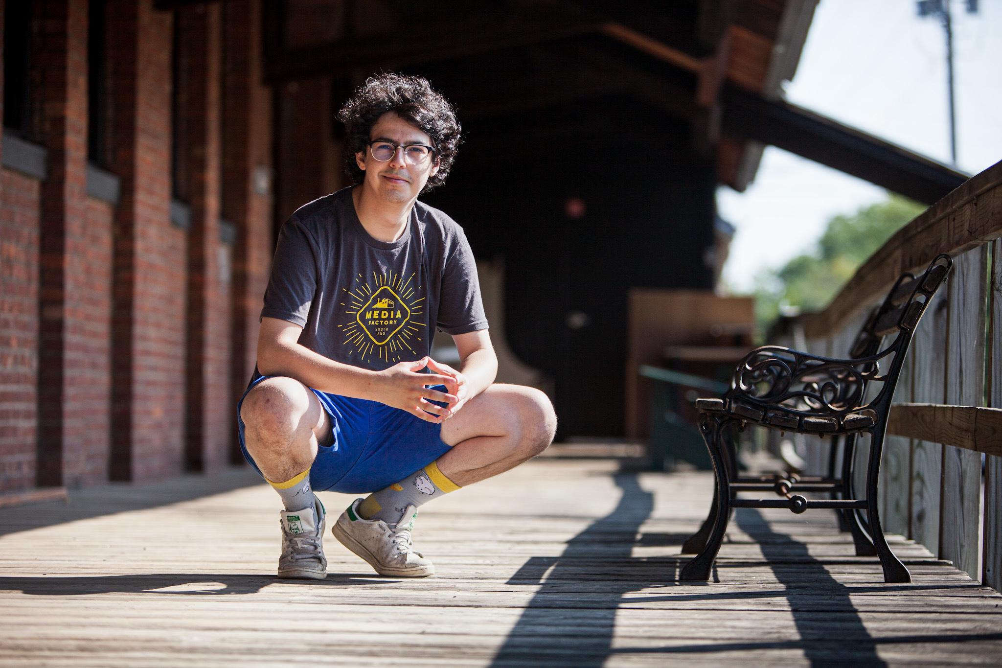 Max Kriff squatting low and smiling at the camera while on the sunny porch of our building