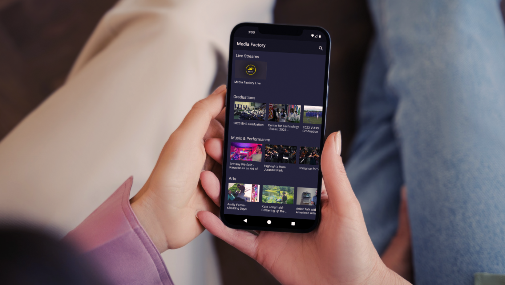 two hands holding a phone with the Media Factory channel visible.