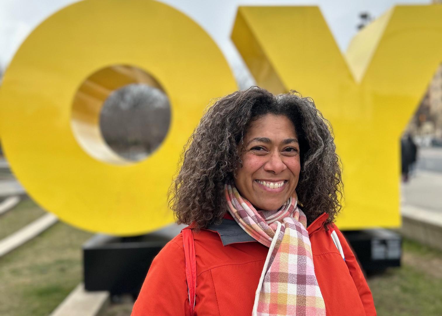 Kendra smiling in a bright red coat in front of large letters "OY."
