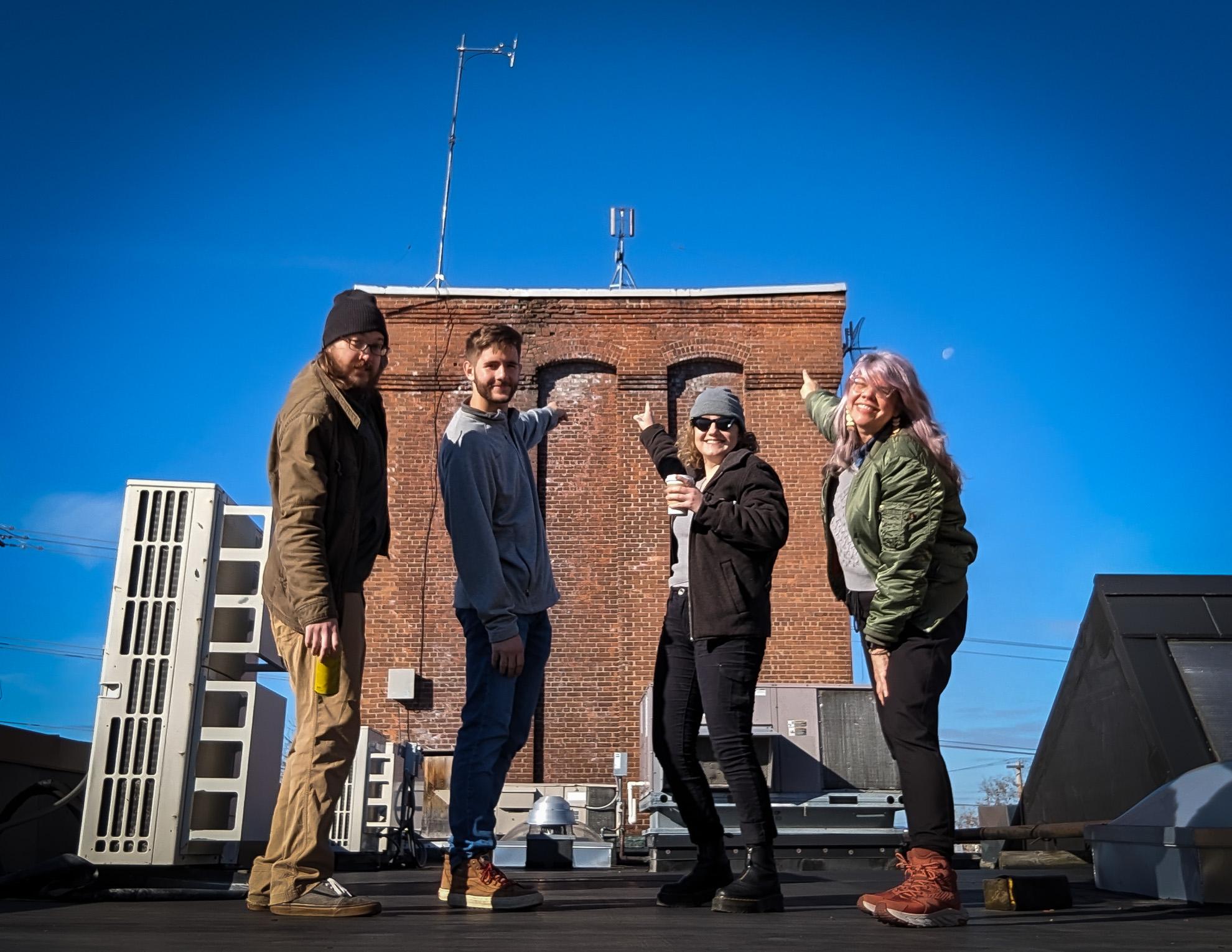 Ross, John, Kate, and Gin on the roof of Media Factory pointing at the radio antennae