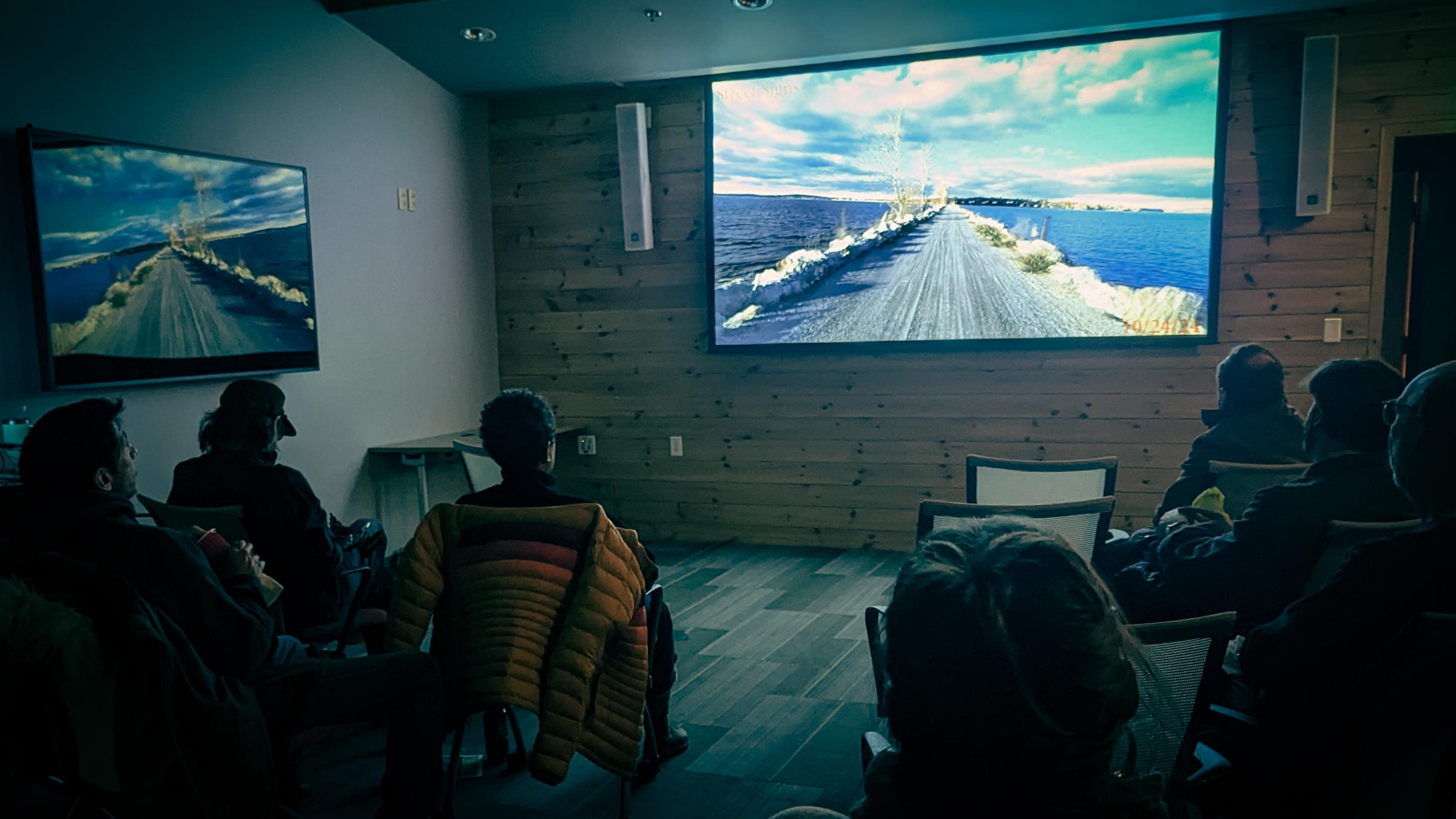 a room full of people watching a video of a bicycle ride on the causeway